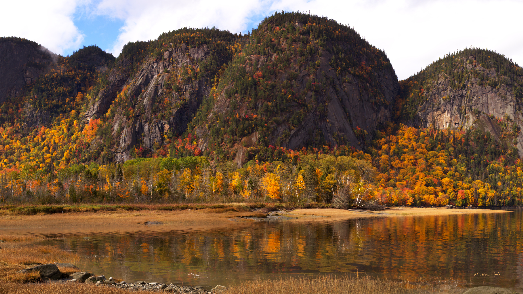 L'automne embrase les falaises millénaires du fjord du Saguenay, reflétées dans le calme des eaux.